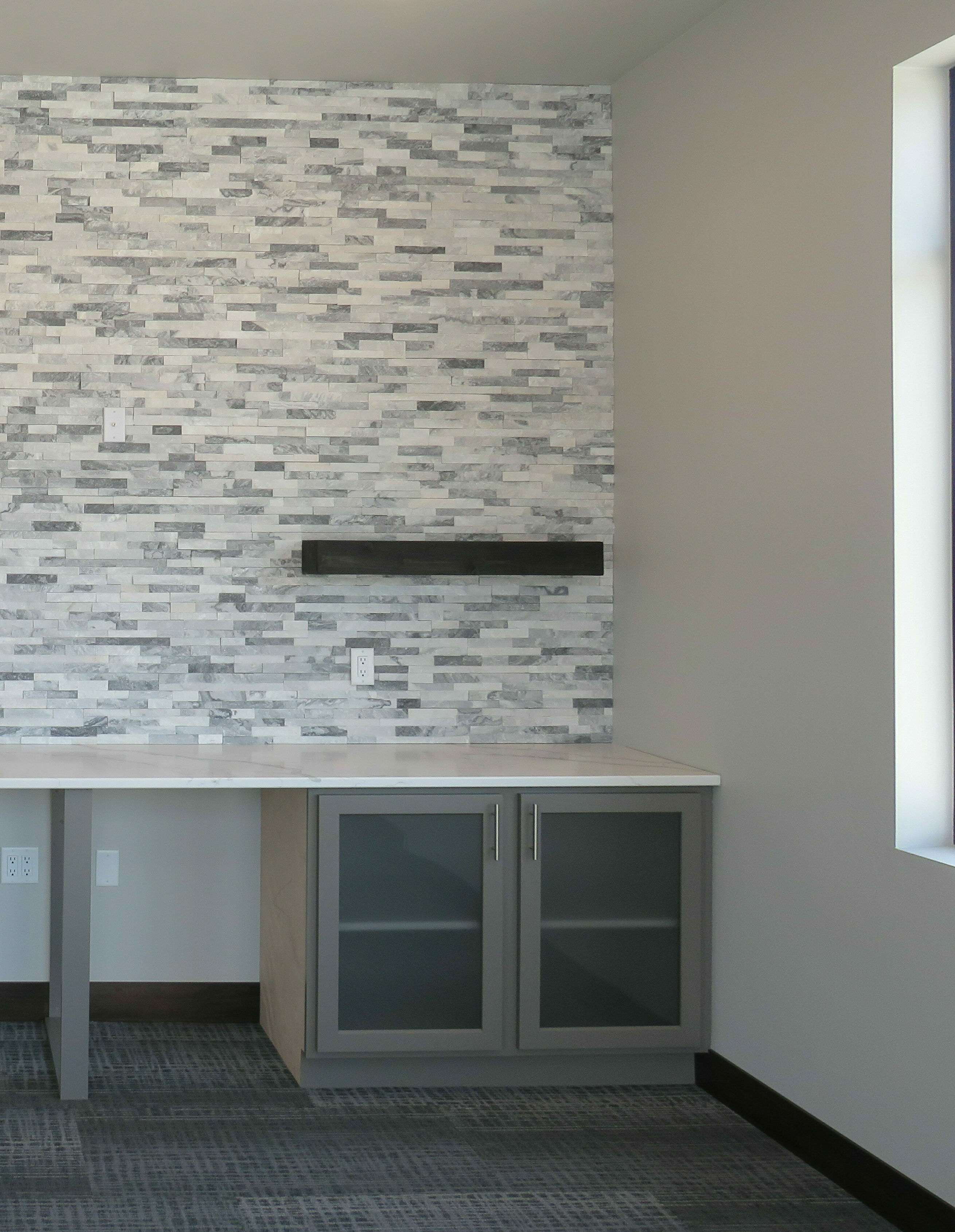 Office meeting room with stone accent wall and floating shelves above grey cabinets and white quartz countertops