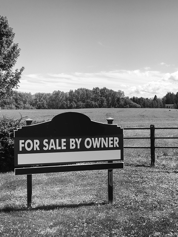 A for sale by owner sign next to an open field ready for development